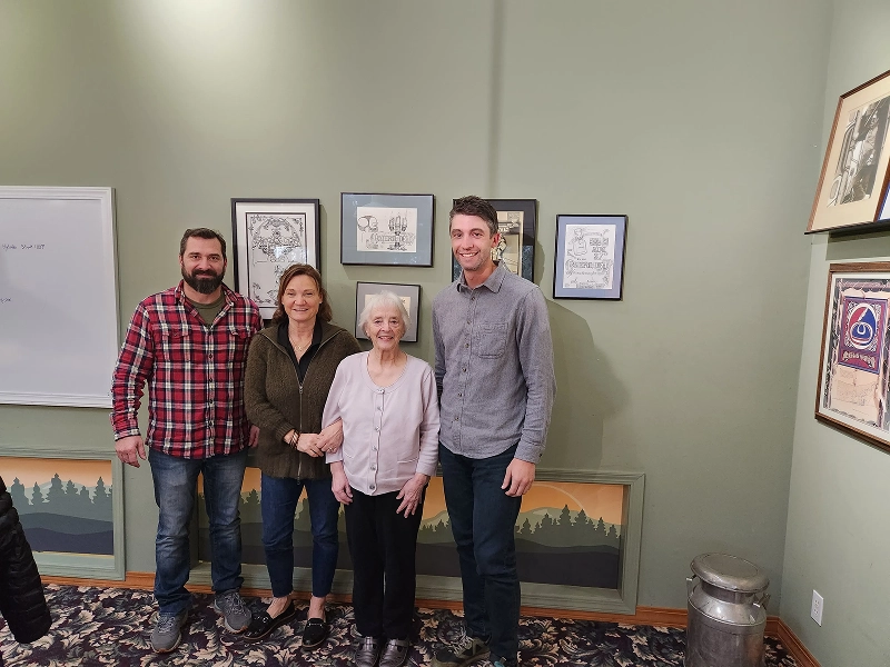 06 Four people standing indoors, smiling for a photo in front of framed art on a green wall.